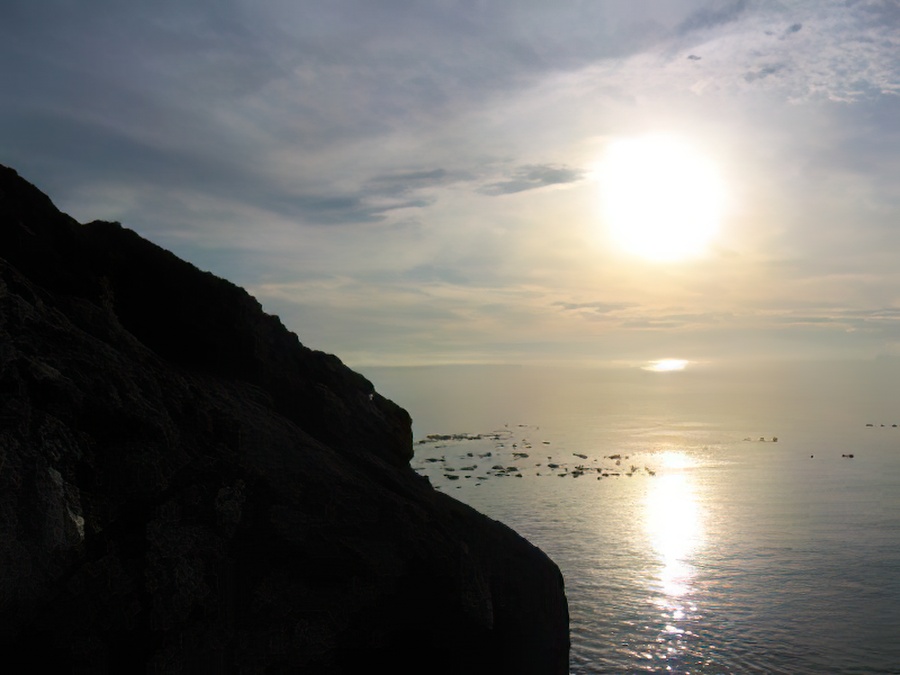A rock cliff into the Salish Sea and the sun low on the horizon.